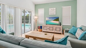 A living room with a pool view, a TV, and a decorative sign on the wall. - Picturesque Island Retreat ~Screened-In Lanai w/ Pool; Central Location w/Beach Gear & WiFi (Marco Island)
