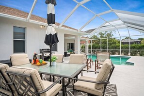 Relax in a spacious patio area with a glass-enclosed pool, comfortable seating, and a grill for outdoor cooking.