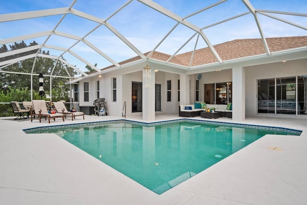 Relax by the pool in a serene, covered outdoor space with a rectangular pool, lounge chairs, and a table.