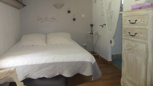 A bedroom with a bed, a dresser, a small table with a lamp, and a wall with a decorative item.