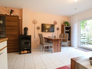 Uma sala de estar moderna com lareira, mesa de jantar com cadeiras, televisão na parede e uma janela grande.