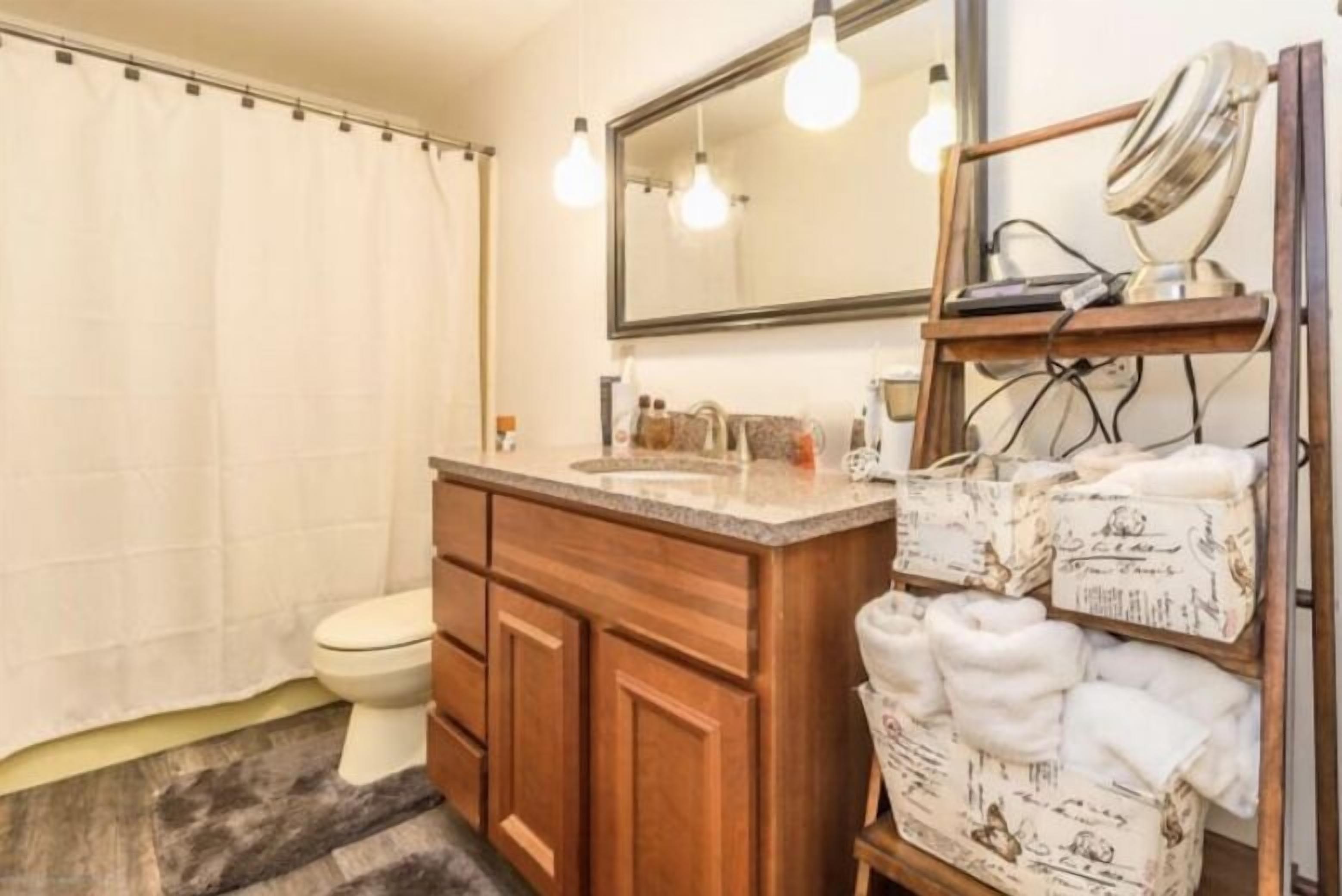 Een badkamer met een houten wastafelmeubel, een grote spiegel en een handdoekrek met handdoeken.