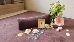 Ein Zimmer mit braunem Teppich, einem kleinen Holzschrank, einer Holzablage mit einer rosa Blume sowie diversen Muscheln und Kristalldekorationen.