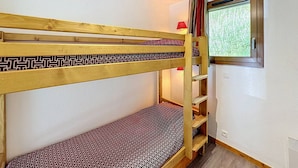 Una cama litera con colchón estampado, una ventana con cortinas y un pequeño estante.