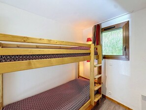 Een stapelbed met een gestreept matras, een raam met gordijnen en een klein wandrek.