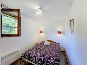 A bedroom with a bed, a window, two wall-mounted lamps, and a mirror.