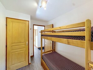 Una habitación con literas, una puerta de madera y un pasillo que conduce a otra estancia.