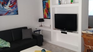 Ein modernes Wohnzimmer mit einer schwarzen Couch, einem weißen Couchtisch, einem Flachbildfernseher und einem kleinen Holztisch mit einem Stuhl.