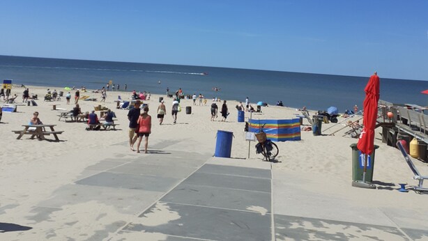 Ein Strand mit Menschen, Picknicktischen und einer Holzpromenade.