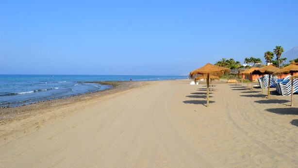 Une plage avec des cabanes à toit de chaume et des parasols de plage rayés.