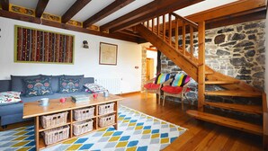 Una sala de estar acogedora con una escalera de madera, una pared de piedra y una alfombra colorida.