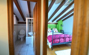 Une chambre à coucher avec un lit, une fenêtre et une vue sur une salle de bain équipée de toilettes et d’un lavabo.
