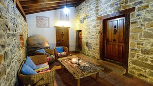 Una habitación acogedora con paredes de piedra, techo de madera, horno de ladrillo, muebles de mimbre y una mesa con velas.