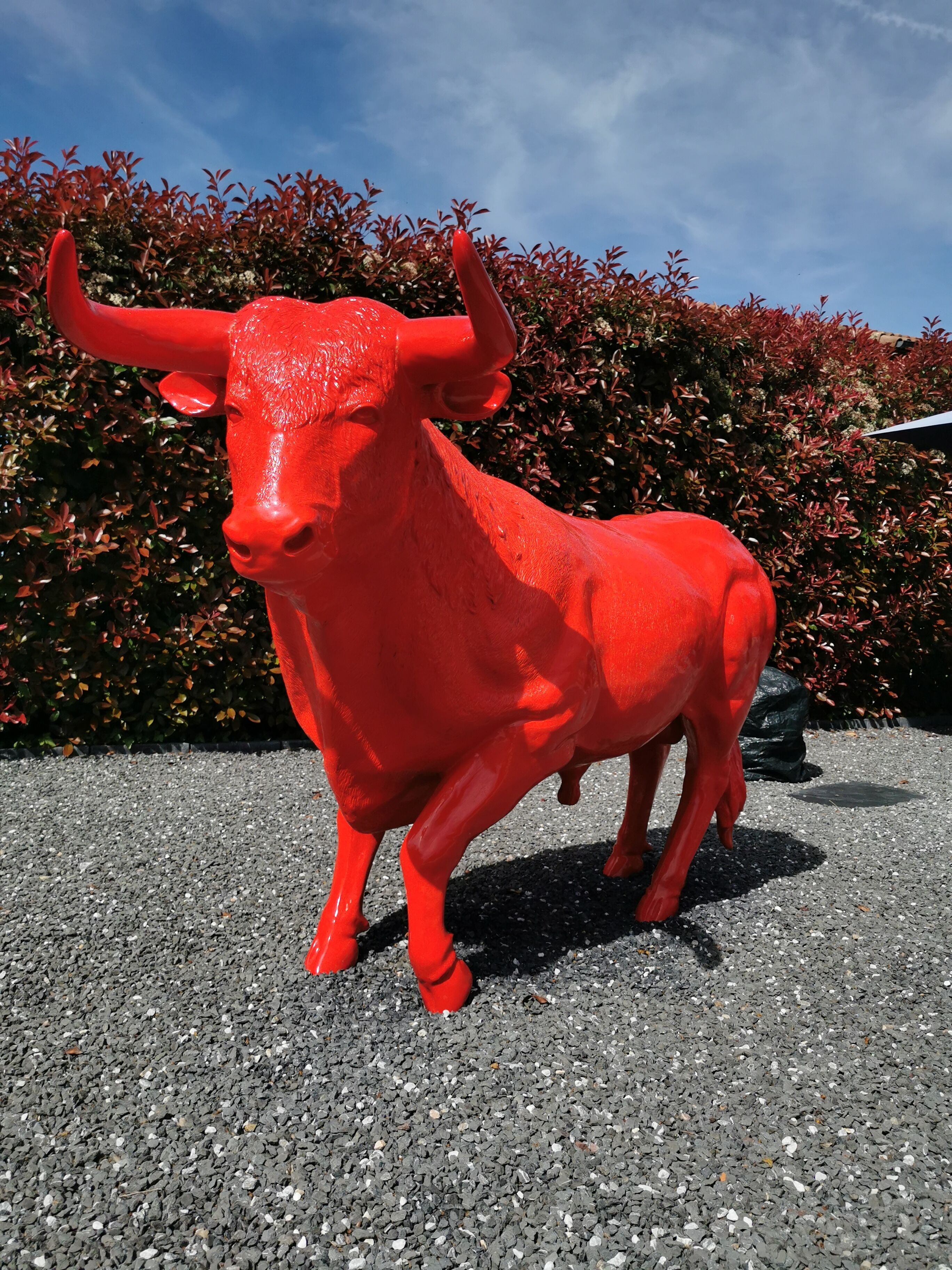 A red bull statue on a gravel surface with a hedge in the background.