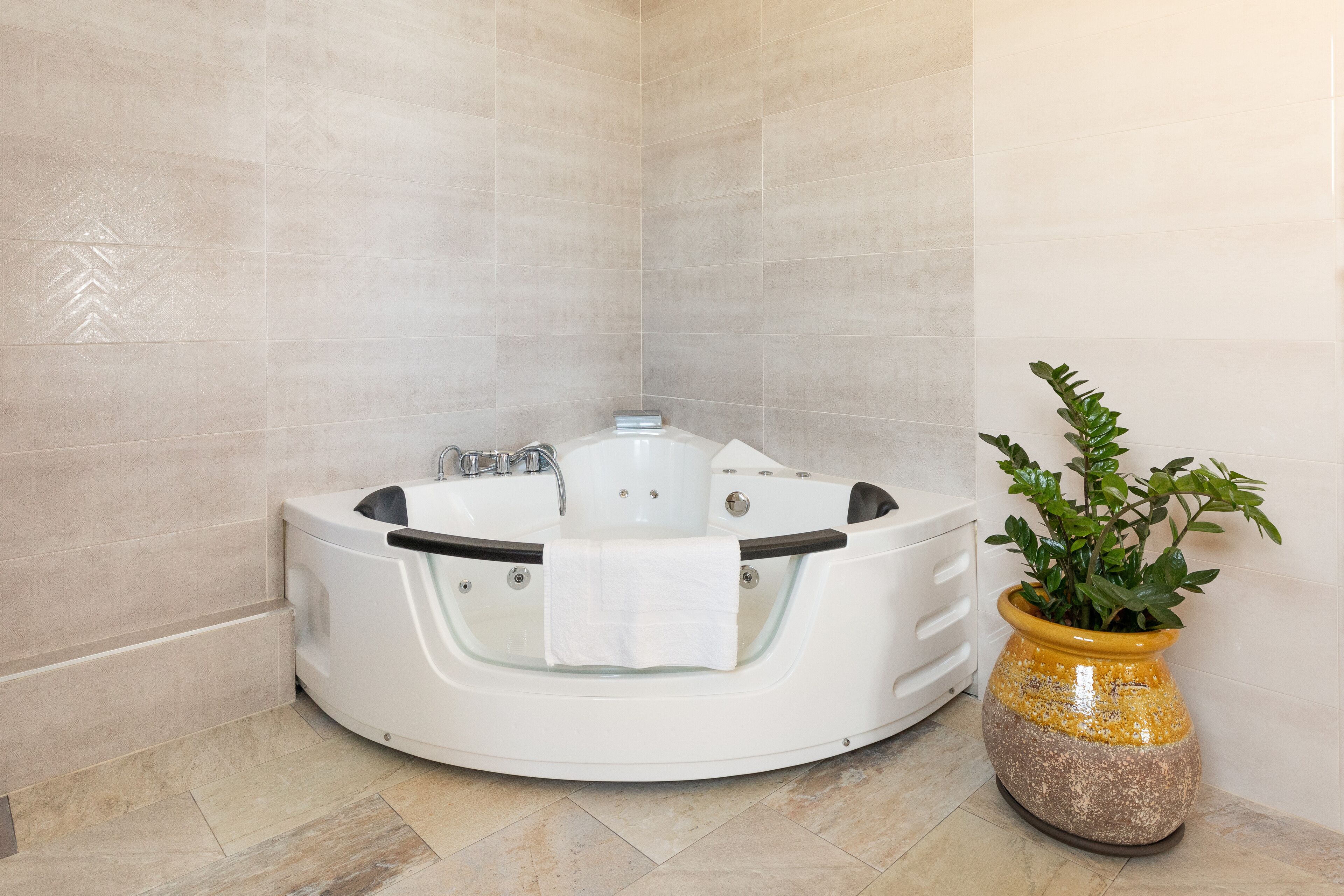 Un baño en esquina con una bañera independiente, una planta en maceta y paredes con azulejos.