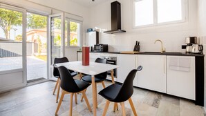 A modern kitchen with white cabinets, a black countertop, and a dining area with a white table and black chairs. - House (Saint Martin de Seignanx)