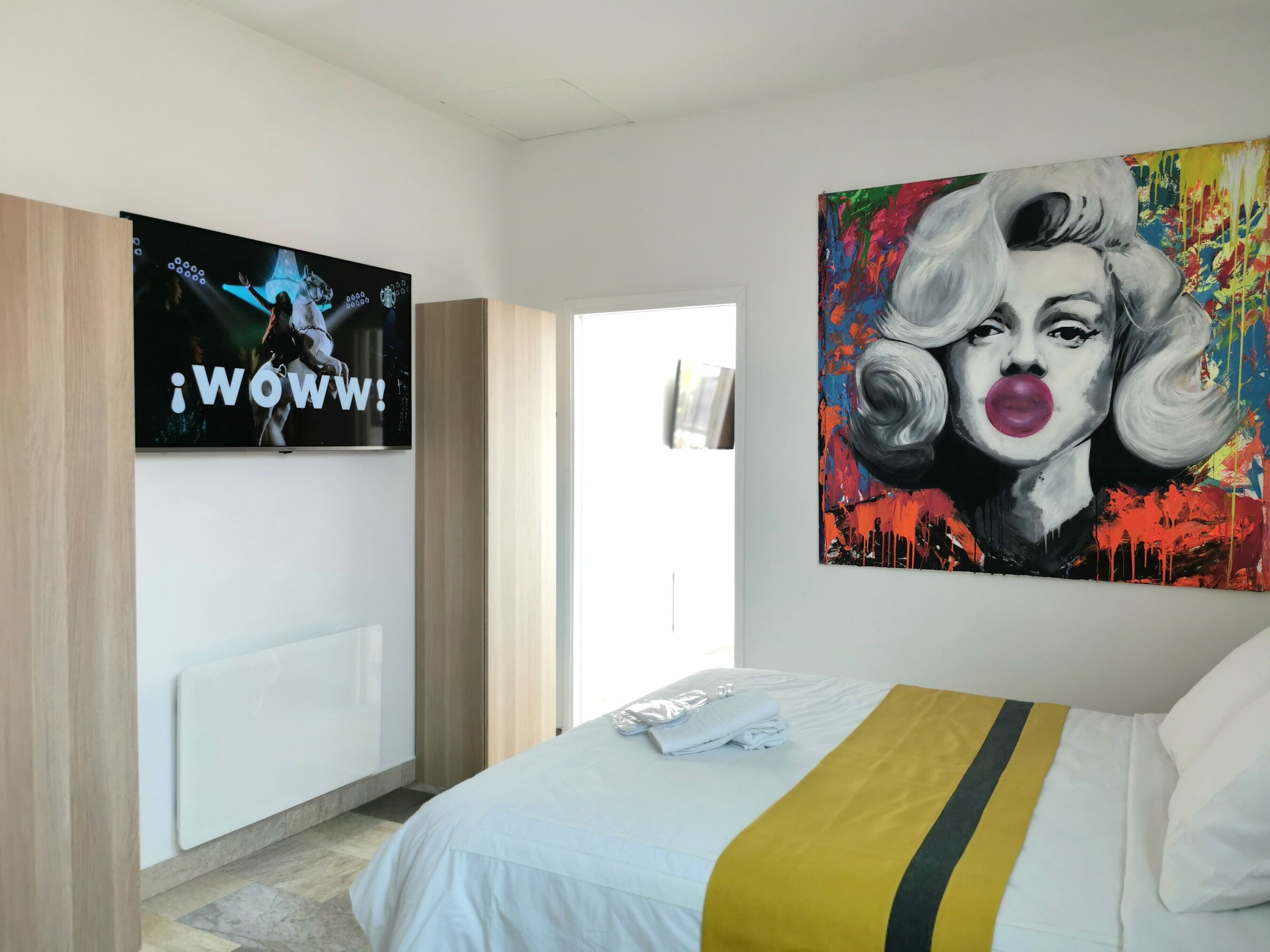 Una camera d'albergo con un letto, una televisione a muro e un quadro.