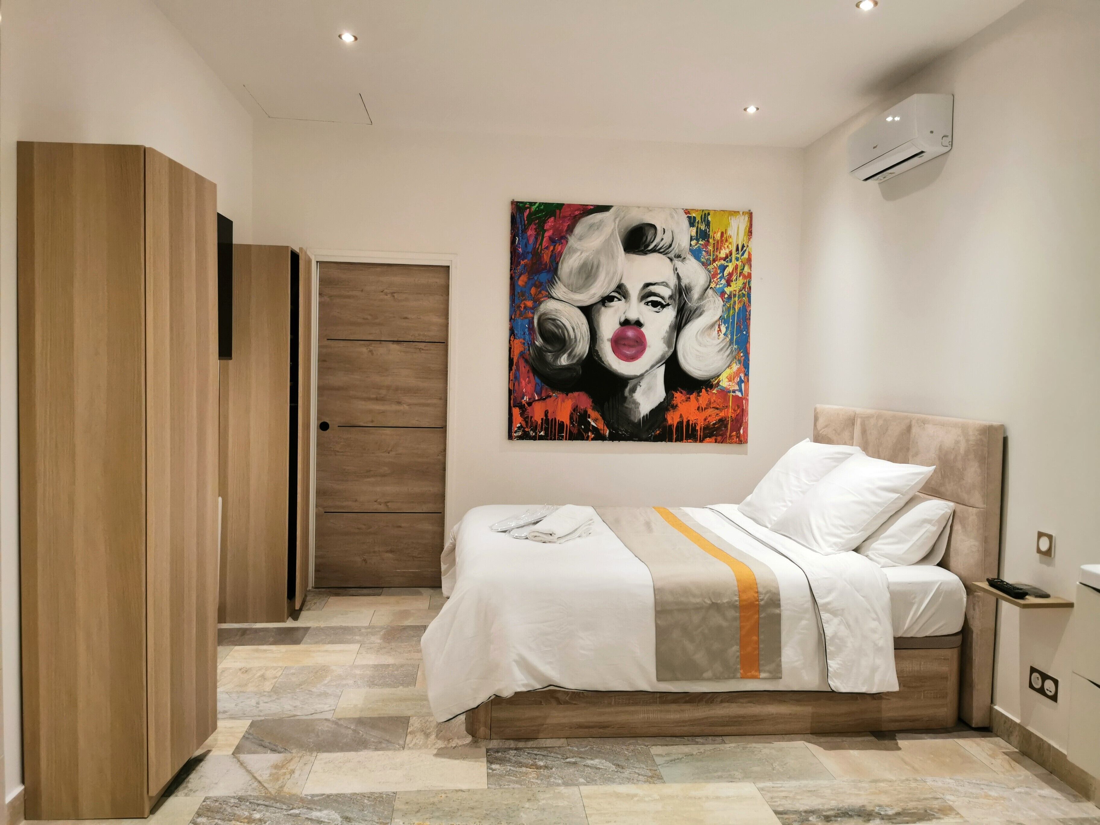 Un dormitorio con cama, armario, un cuadro y aire acondicionado.