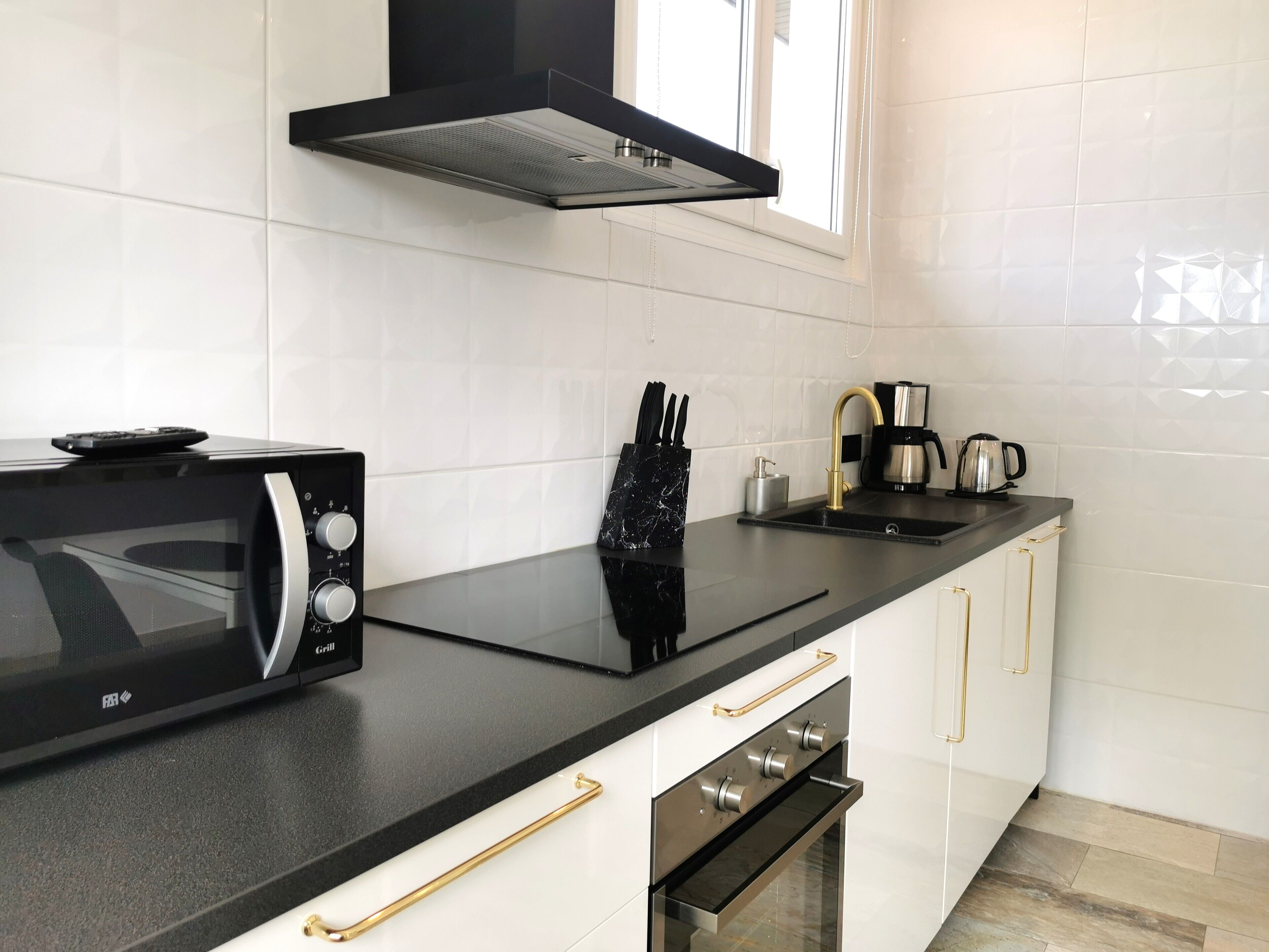 Una cocina moderna con encimera negra, armarios blancos, horno empotrado, microondas, cafetera y campana extractora negra.