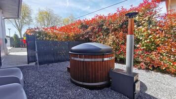 A hot tub with a wooden exterior and a metal base, surrounded by gravel and a wooden fence.