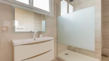 Een moderne badkamer met een douchecabine van glas, een witte wastafel met spiegel en een lichtgekleurde betegelde vloer.