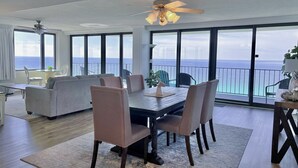 A modern living room with a dining area, large windows, and a view of the ocean. - Picturesque Beachfront Condo- Spacious  Balcony, 2BD/2BA, Pool & Tiki Bar (panama city beach)