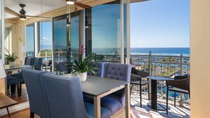 A modern dining area with a view of the ocean, featuring a table and chairs, a ceiling fan, and a potted plant. - CORNER Unit with 11th Floor Waikiki Ocean, Lagoon & Marina Views! Washlet! (Honolulu)