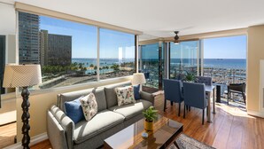 A modern living room with a large window offering a view of the marina and ocean. - CORNER Unit with 11th Floor Waikiki Ocean, Lagoon & Marina Views! Washlet! (Honolulu)