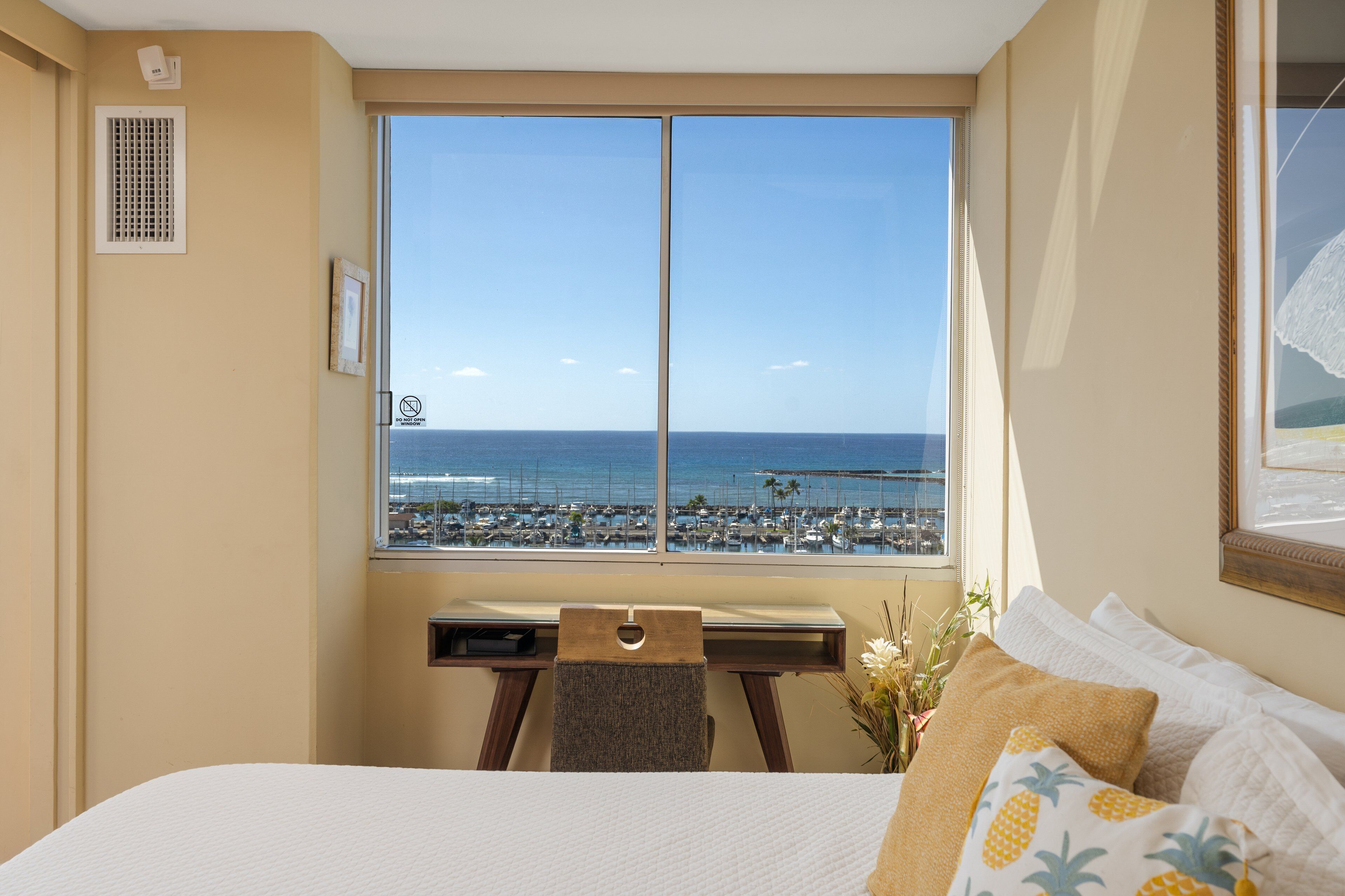 A hotel room with a large window offering a view of the beach and marina.