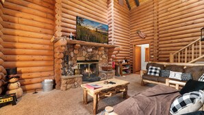 A log cabin interior with a stone fireplace, a wooden sofa, a coffee table, and a television mounted above the fireplace. - Adorable 1,500 sq ft log cabin, HOT TUB! Close to Lake, Village, & Forest! (Big Bear Lake)