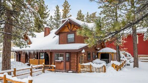 A log cabin with a wooden porch and snow-covered surroundings. - Adorable 1,500 sq ft log cabin, HOT TUB! Close to Lake, Village, & Forest! (Big Bear Lake)