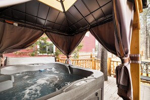 A hot tub with a wooden deck and a red building in the background. - Log Cabin with Hot Tub | Across from Aspen Glen | Near Village & Lake (Big Bear Lake)