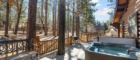 A deck with a hot tub, wooden deck, and surrounding trees.
