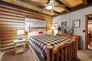 A log cabin-style bedroom with a bed, wooden headboard, ceiling fan, and wall-mounted TV. - Log Cabin with Hot Tub | Across from Aspen Glen | Near Village & Lake (Big Bear Lake)