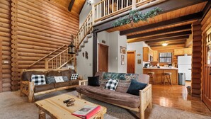 A log cabin interior with a living room, kitchen, and a staircase leading to a loft. - Adorable 1,500 sq ft log cabin, HOT TUB! Close to Lake, Village, & Forest! (Big Bear Lake)