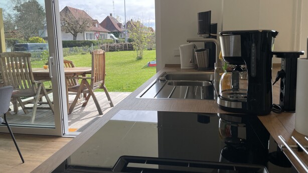 A modern kitchen with a large window, a coffee maker, and a dining area with wooden furniture.