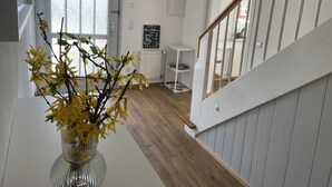 A hallway with a wooden floor, a white staircase, and a vase with yellow flowers on a white table.
