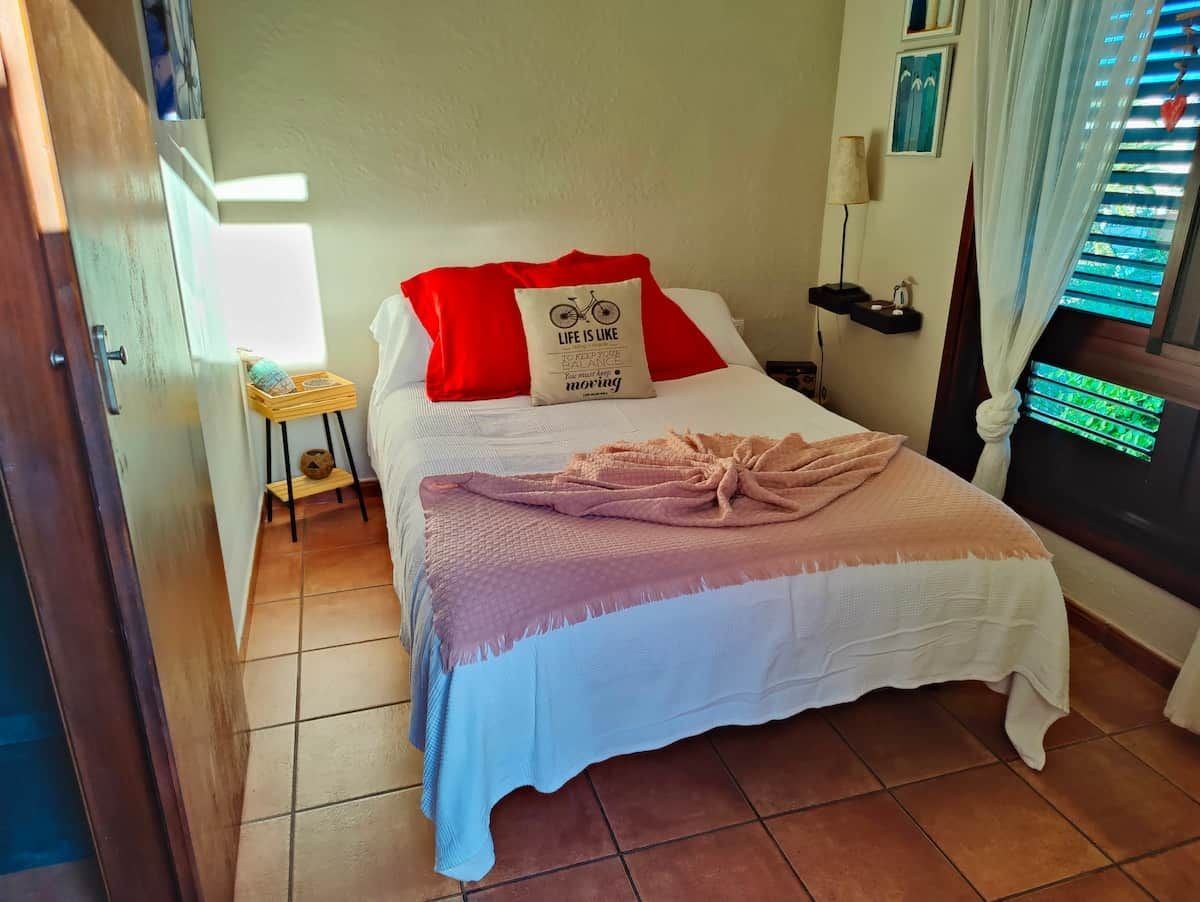 Ein Schlafzimmer mit Bett, Kissen, einem Nachttisch und einem Fenster mit Vorhängen.