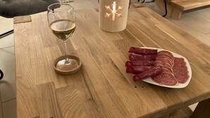 Una mesa de madera con una copa de vino blanco, una vela y un plato de salami en rodajas.