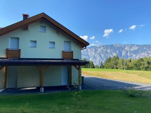 A two-story house with a sloped roof, wooden balcony, and a view of mountains in the background.
