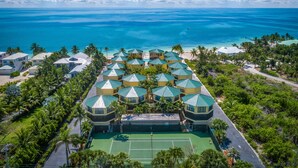Vue aérienne d’un complexe hôtelier comprenant plusieurs bâtiments, un court de tennis et une plage.