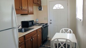 A compact kitchen with wooden cabinets, a white refrigerator, a microwave, and a stove. - Shore Bird - 1 BR Studio Cottage with open floor plan. NO LINENS PROVIDED (Chincoteague Island)