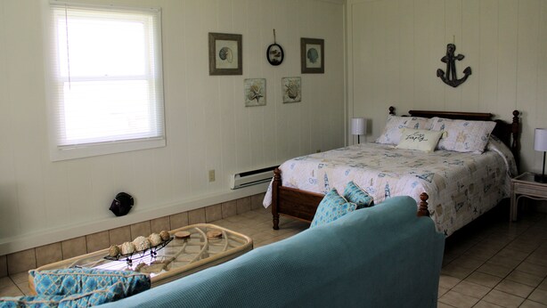 A bedroom with a bed, a ceiling fan, a window, and wall decorations. - Shore Bird - 1 BR Studio Cottage with open floor plan. NO LINENS PROVIDED (Chincoteague Island)