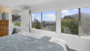 A bedroom with a large window, a bed, a dresser, and a lamp. - 124H Unit 2: Cozy 2 Bedroom Unit, Stunning Views, BBQ, GOLF CART (Avalon)