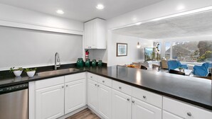 A modern kitchen with white cabinets, a stainless steel dishwasher, and a black countertop. - 124H Unit 2: Cozy 2 Bedroom Unit, Stunning Views, BBQ, GOLF CART (Avalon)