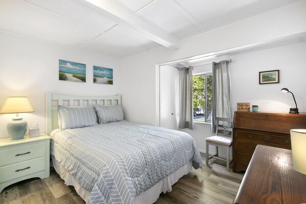 Een slaapkamer met een bed, nachtkastje, kapstok en een raam met gordijnen.