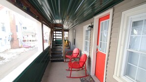 A covered porch with a red door, two rocking chairs, and a view of the street. - 6BR Downtown Duplex Walk to Gore & Main St | Porches, Game Room | Sleeps 12 (North Creek)