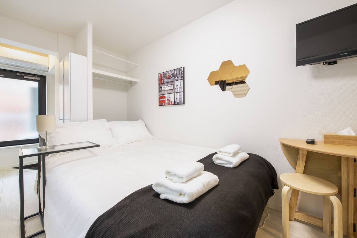 Habitación de hotel con cama, escritorio, silla, televisor y ventana.