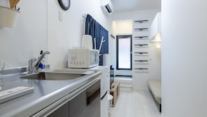 Cocina compacta con microondas, pileta y alacenas. Cuenta con un pequeño rincón de descanso con un banco y una lámpara.