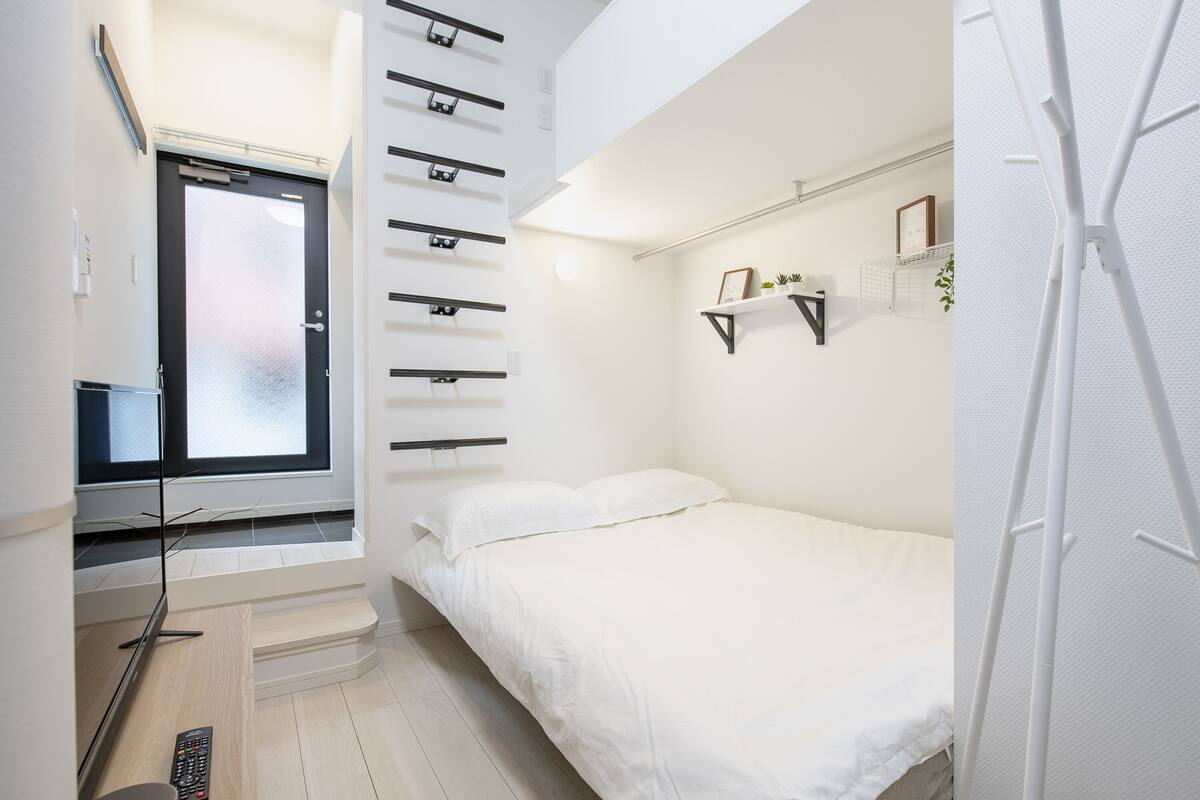 Un dormitorio moderno con una cama, un televisor, una ventana y una estantería con plantas.